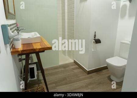 Bagno pulito e contemporaneo con lavandino in legno in stile rustico, lavandino, WC bianco e doccia piastrellata della metropolitana Foto Stock