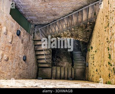 Una vista che si affaccia su una stretta scala a chiocciola in pietra all'interno di una storica torre medievale, catturando l'elegante geometria e l'antico design architettonico. Foto Stock