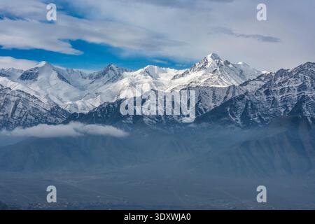 Le cime innevate della catena montuosa Stok Range, con la vetta prominente di Stok Kangri, si innalzano sopra uno strato di basse nuvole in lontananza a Leh. Foto Stock