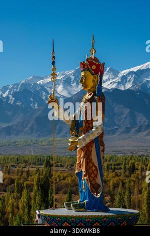 Un profilo a tutta lunghezza della colorata statua di Guru Padmasambhava a Shey si affaccia su una valle di alberi autunnali con alte cime montuose in lontananza. Foto Stock