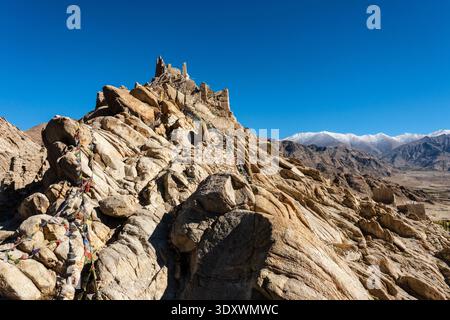 Antiche rovine di mattoni di fango del Palazzo Shey in cima a un'aspra collina sotto un cielo blu cristallino con la catena montuosa del Ladakh innevata in lontananza. Foto Stock