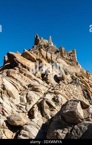 Antiche rovine di mattoni di fango del Palazzo Shey in cima a un'aspra collina sotto un cielo blu cristallino con la catena montuosa del Ladakh innevata in lontananza. Foto Stock