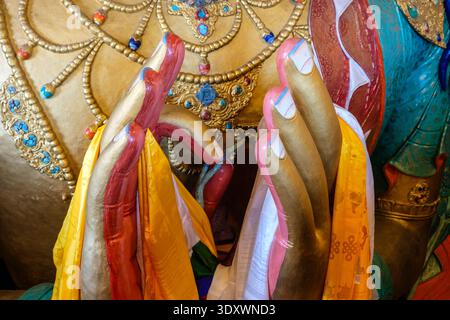 Primo piano delle mani del Buddha Maitreya a Thiksey Gompa, adornato da colorate sciarpe di seta e intricati dettagli di gioielli dorati. Foto Stock