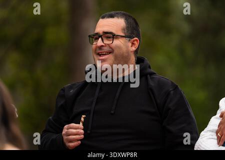 Uomo in una felpa nera con cappuccio sorridente e in mano un bastoncino di caramelle a righe all'aperto Foto Stock