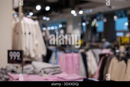 interni sfocati di un moderno negozio di moda che mostra scaffali di abbigliamento colorati e cartellini dei prezzi con soffice illuminazione bokeh per uno sfondo di shopping Foto Stock