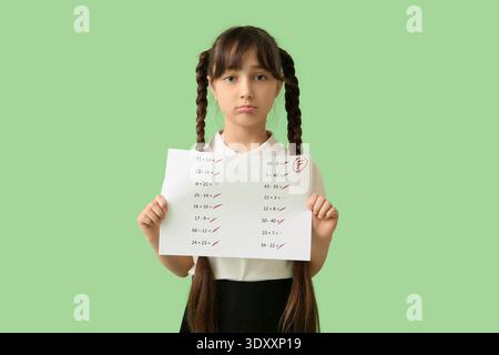 Triste studentessa che tiene carta con risultati negativi del test scolastico su sfondo verde Foto Stock