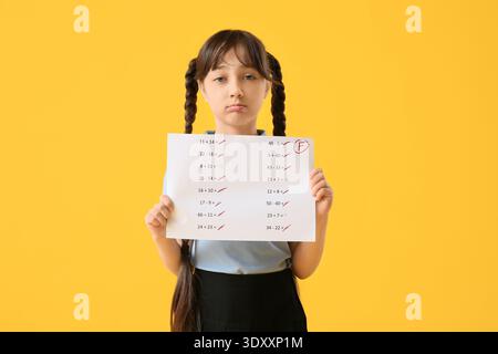 Una studentessa triste che ha i risultati negativi del test scolastico su sfondo giallo Foto Stock