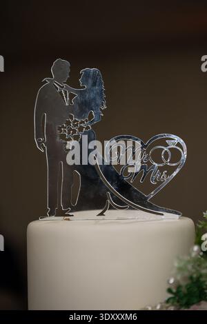 Topper per torta nuziale "Mr. & Mrs." in acrilico a specchio argentato tagliato al laser, caratterizzato da una silhouette da sposa e sposo e anelli a incastro all'interno di un cuore. Foto Stock
