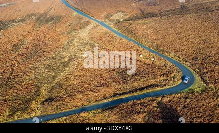 Veduta aerea di un'auto argentata che attraversa una curva a gomito su una brughiera Foto Stock