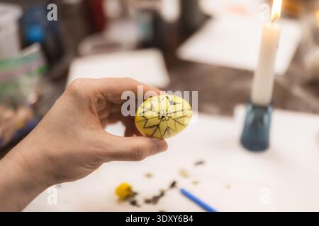 La mano tiene in mano un uovo giallo con un intricato design a stella nera durante una lezione della comunità per la creazione di uova pisanky ucraine (uova colorate e decorative con artwo Foto Stock