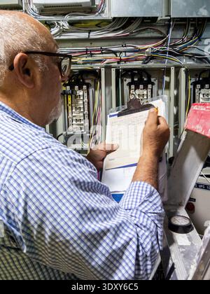 Elettricista senior che installa interruttori automatici all'interno del quadro di comando elettrico Foto Stock