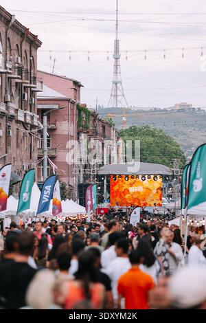 Folla di visitatori che camminano attraverso la strada trafficata durante il festival Yerevan Wine Days con un palco di concerti sullo sfondo e la torre della televisione Foto Stock