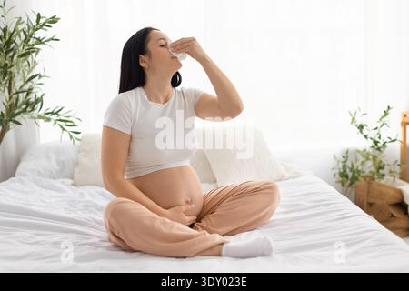 Donna incinta che soffia il naso con tessuti mentre si sente male a casa Foto Stock