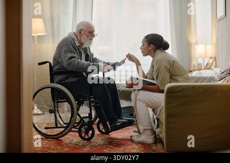 Donna nera lavoratrice sociale che assiste l'uomo caucasico anziano in sedia a rotelle Foto Stock