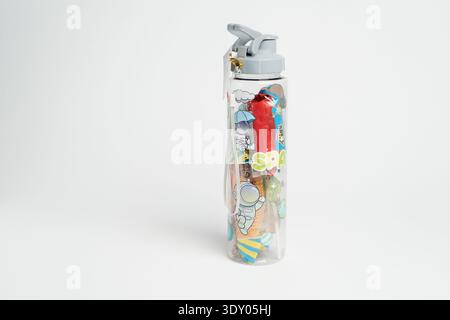 Bottiglia d'acqua per bambini in plastica trasparente con coperchio grigio ribaltabile, stampa colorata a tema cartoon spaziale, isolata su sfondo bianco nell'illuminazione da studio. Foto Stock