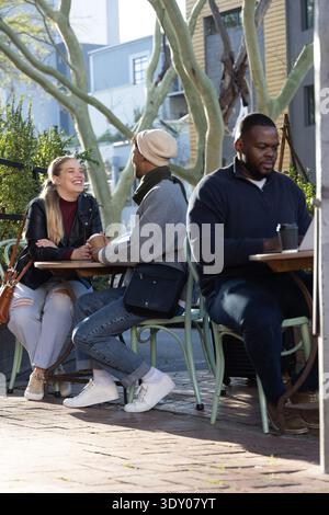 Coppia che ride e si piega, tenendosi per mano nel patio della caffetteria sul lato della strada con un computer portatile nelle vicinanze. Esterno, terrazza, marciapiede, Unione, conversazione, JOY, Coffee || modello rilasciato Foto Stock