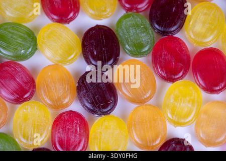 Il primo piano di caramelle dure multicolore rivela una texture lucida e forme circolari disposte a ripetizione su sfondo bianco, con contrasto elevato Foto Stock