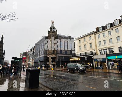 Edimburgo, Scozia, Regno Unito - 15 febbraio 2026: I pedoni passano davanti a negozi e autobus in una giornata umida e coperta lungo Princes Street a Edimburgo. Foto Stock