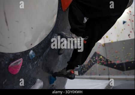 Una foto dettagliata dei piedi di un atleta con scarpe da arrampicata specializzate e pantaloni neri che si allenano su una parete. Il colore grigio e colorato si fondono in un moderno Foto Stock