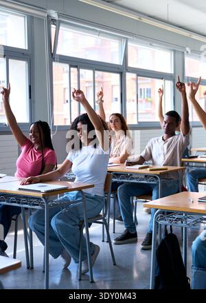 Gruppo di studenti diversi che alzano la mano in un'aula luminosa Foto Stock