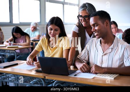 Insegnante che aiuta diversi studenti con un notebook in classe Foto Stock