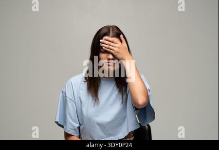 Giovane donna che soffre di forte mal di testa o emicrania, si sente stressata, frustrata e delusa, coprendo il viso con la mano Foto Stock