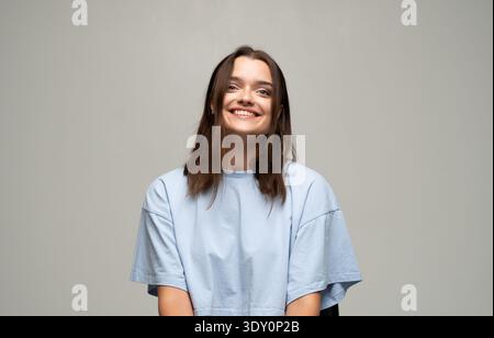 Giovane donna sorridente, che esprime genuina felicità, gioia ed emozioni positive in un contesto neutrale Foto Stock