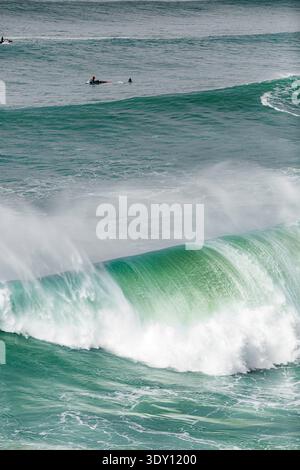 Onde vibranti si schiantano con una forza potente. I surfisti scivolano su acque lontane e calme. Nebbia e schiuma si mescolano nel mare turchese. Energia e movimento definiscono l'oc Foto Stock