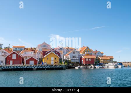 Case sul lungomare e banchina con piccole barche nel canale del porto nel tradizionale villaggio di pescatori di Grundsund sull'isola di Ösö, Bohuslän, costa occidentale della Svezia Foto Stock
