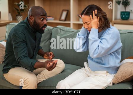 Coppia adulta multirazziale seduta sul divano nel loro appartamento e con una disputa. Sono arrabbiati l'uno con l'altro. Foto Stock