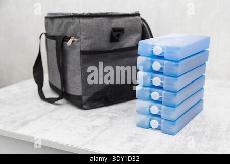 Pila di elementi di raffreddamento blu sulla superficie leggera. Borsa termica isolata grigia posizionata dietro. Configurazione per il controllo portatile della temperatura di alimenti e bevande Foto Stock