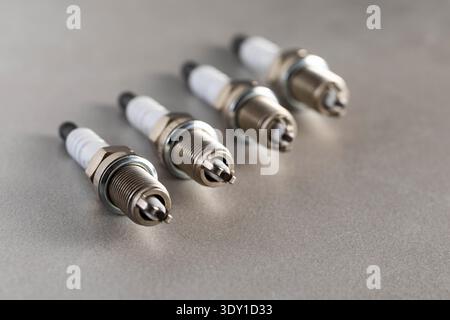 Vista ravvicinata di quattro nuove candele per auto allineate su una superficie ruvida grigio chiaro. Componenti essenziali per il sistema di accensione del motore e affidabili Foto Stock