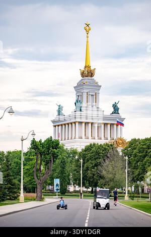 Mosca, Russia - 25 agosto 2025: Padiglione centrale VDNKh Mosca con bandiera russa e strada trafficata del parco Foto Stock