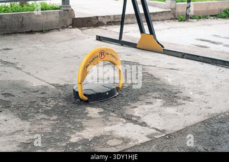 Un bagagliaio giallo con il cartello "No Parking" è fissato su una superficie asfaltata sporca in un'area di parcheggio. Foto Stock