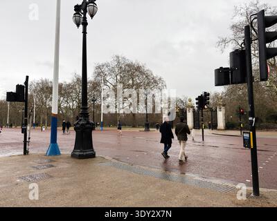 Londra, Regno Unito - 1 febbraio 2026: I pedoni attraversano una strada della città bagnata dalla pioggia a Londra accanto a cancelli ornati e classici lampioni. Foto Stock
