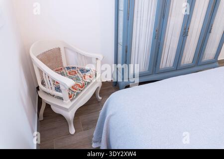 Gli interni della camera da letto presentano una poltrona bianca decorativa e una credenza blu vintage che creano un'atmosfera accogliente e invitante Foto Stock