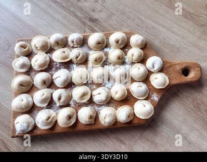 Gnocchi crudi fatti in casa su tagliere di legno con farina. Processo di cottura tradizionale, vista dall'alto, luce naturale, cucina rustica. Foto Stock