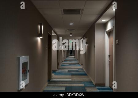 Lungo corridoio dell'hotel con porte, illuminazione e segnali di uscita. Foto Stock