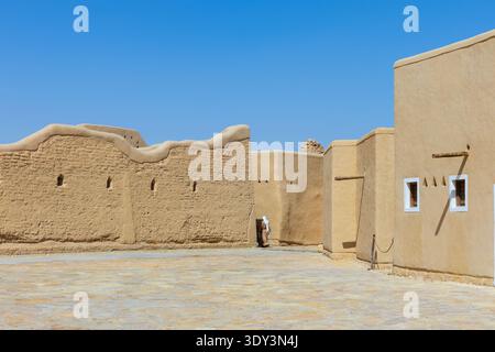 Un uomo saudita in abbigliamento tradizionale passeggia davanti a case restaurate in mattoni di fango (architettura Najdi) nel distretto di AT-Turaif a Diriyah, Arabia Saudita Foto Stock