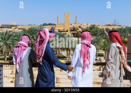 Quattro uomini in tradizionale abbigliamento saudita che puntano alle rovine del sito archeologico del distretto di at-Turaif a Diriyah, Arabia Saudita Foto Stock