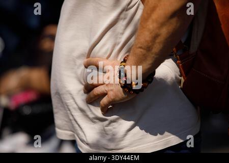 Uomo anziano in piedi mano sull'anca, momento di strada candid, scena all'aperto spontanea, movimento naturale, pelle della mano, primo piano, Wat Pho. Foto Stock