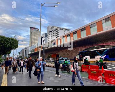 Giacarta, Indonesia - 5 marzo 2026: I pendolari camminano lungo un marciapiede affollato accanto a autobus e motociclette nel centro di Giacarta durante l'ora di punta serale. Foto Stock