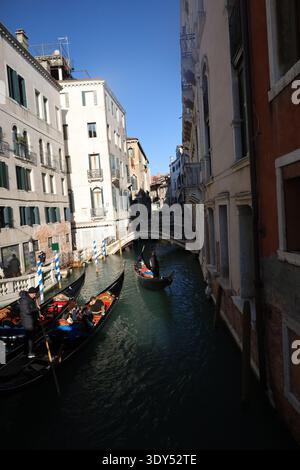 Le gondole viaggiano lungo un canale delimitato da edifici storici, con la luce del sole che emette un forte contrasto sulle facciate e sui riflessi nell'acqua. Foto Stock