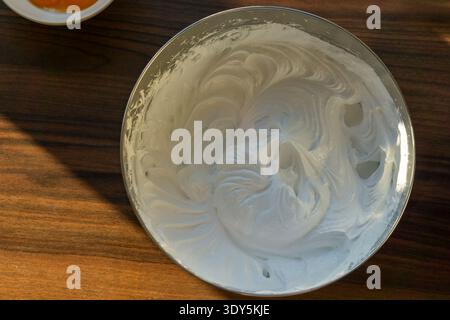 Vista dall'alto della spessa meringa lucida appoggiata su un tavolo di legno in una ciotola in acciaio inossidabile. Foto Stock