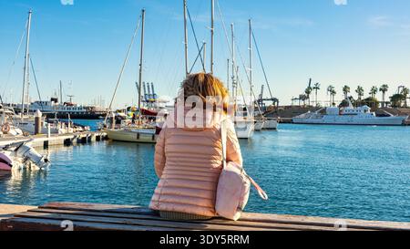Donna seduta su una panchina che riposa guardando le barche nel porto di Valencia. Foto Stock