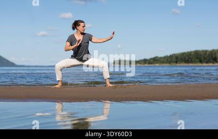 Donna che pratica tai chi chuan e yoga sulla spiaggia. Capacità di gestione cinese QIS energia. attività individuali all'aperto. Distanziamento sociale || modello rilasciato Foto Stock
