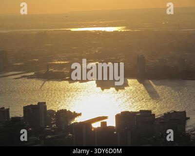 Una vista panoramica del tramonto mostra alti edifici lungo un lungomare che proiettano lunghe ombre attraverso l'acqua scintillante. Foto Stock
