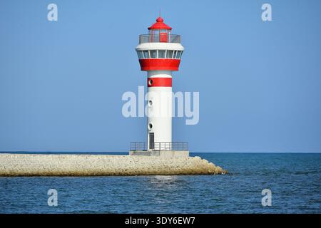 Un faro a strisce rosse e bianche si erge alto lungo la riva del mare. Foto Stock