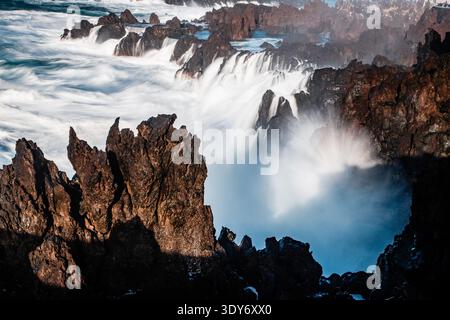 Le onde si schiantano contro le coste rocciose di Porto Moniz Madeira durante una potente dimostrazione della forza della natura in una giornata di sole Foto Stock