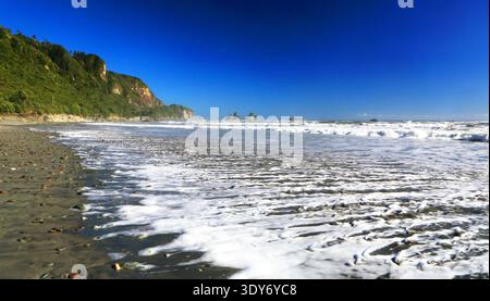 Le onde si infrangono sulla riva mentre la luce del sole splende sulla spiaggia vicino a Great Coast Road nell'Isola del Sud della nuova Zelanda Foto Stock